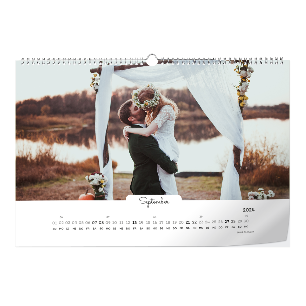 Kalenderblatt September zeigt Braut im Hochzeitskleid und Bräutigam unter einer Blumengirlande am Seeufer umarmt.